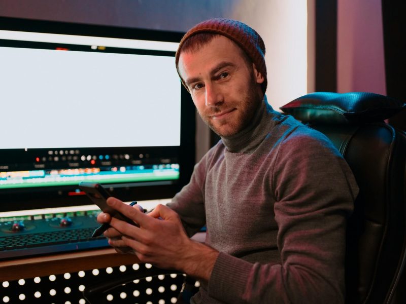 male-video-editor-sitting-at-his-computer-using-phone-1.jpg